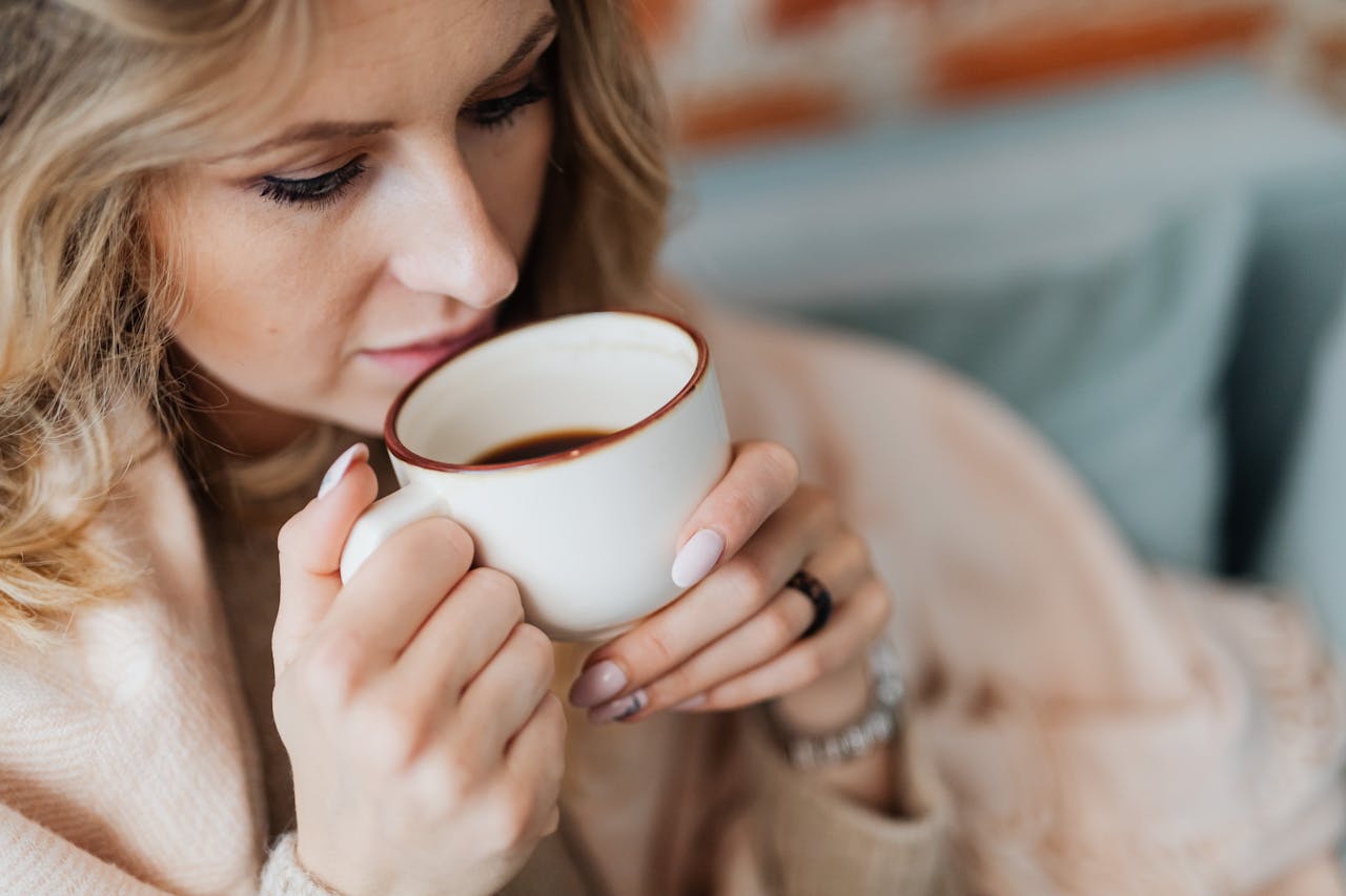 Close-up of a woman savoring a hot coffee cup while relaxing indoors, capturing a cozy moment.